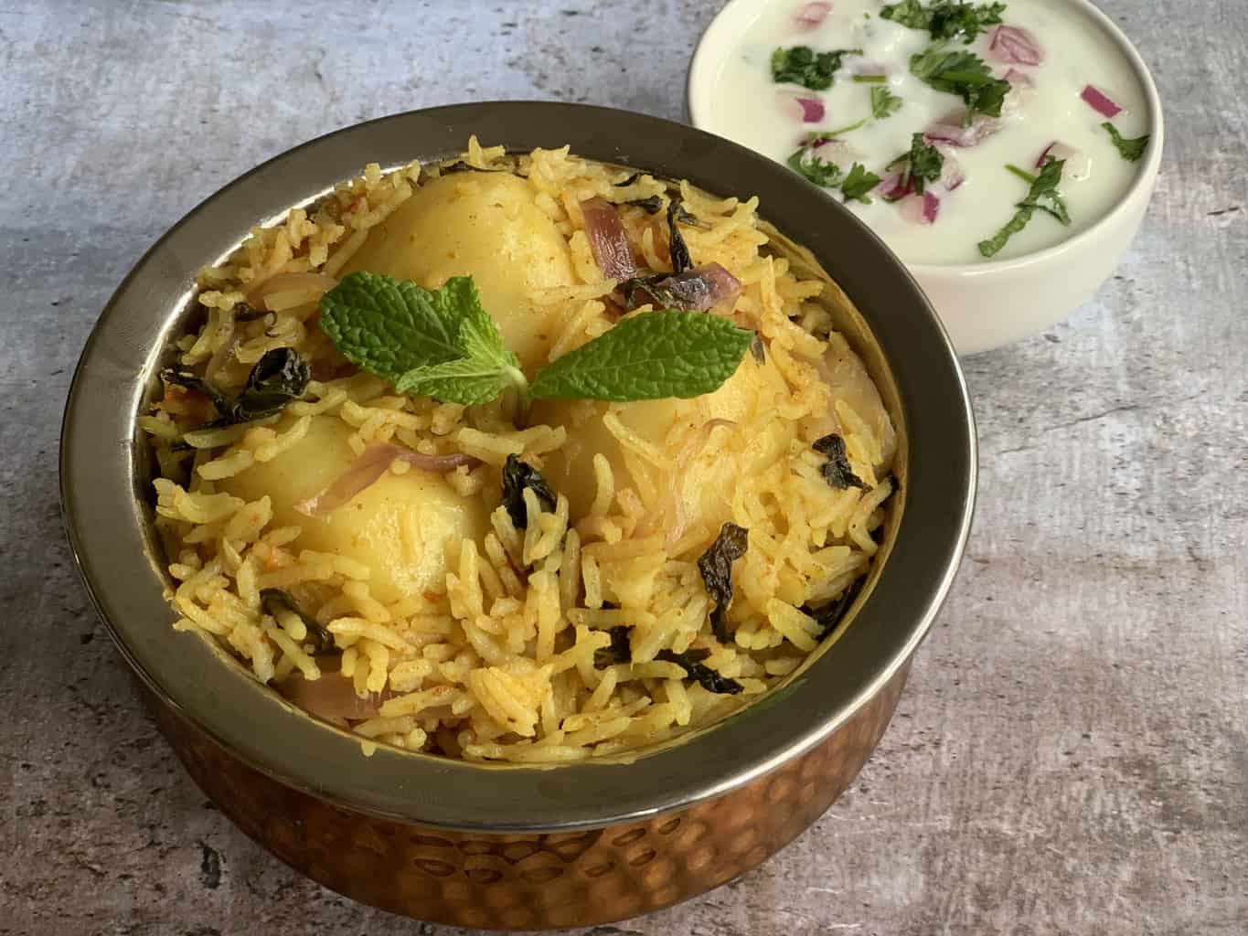 Potato Biryani served in a handi garnished with mint with side of raita