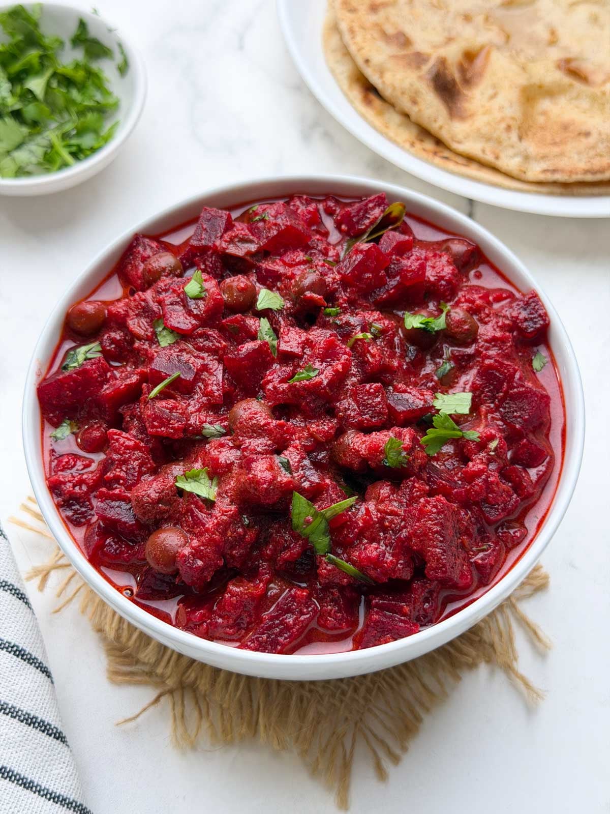 Beetroot kurma karnataka style served in a white bowl with chapati and coriander on the side.