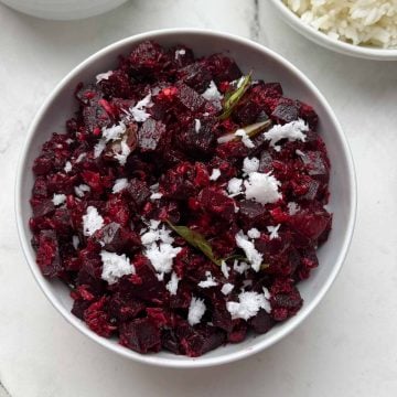 beetroot poriyal served in a white bowl garnished with fresh coconut with rice and rasam on the side.