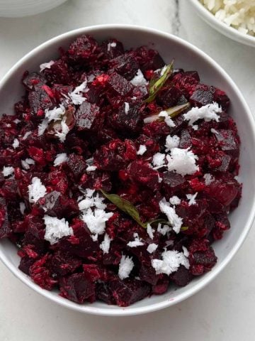 beetroot poriyal served in a white bowl garnished with fresh coconut with rice and rasam on the side.