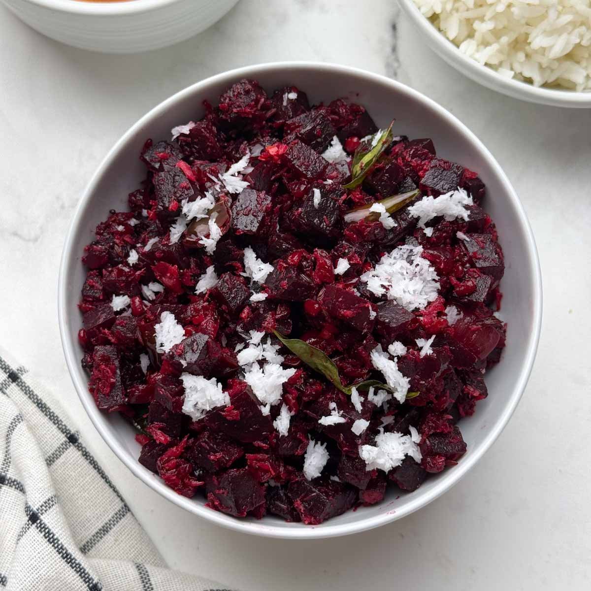 beetroot poriyal served in a white bowl garnished with fresh coconut with rice and rasam on the side.