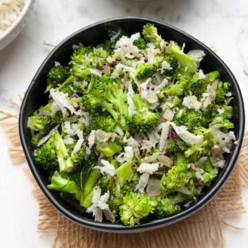 broccoli poriyal served in a black bowl with steamed rice and tomato rasam on the side.