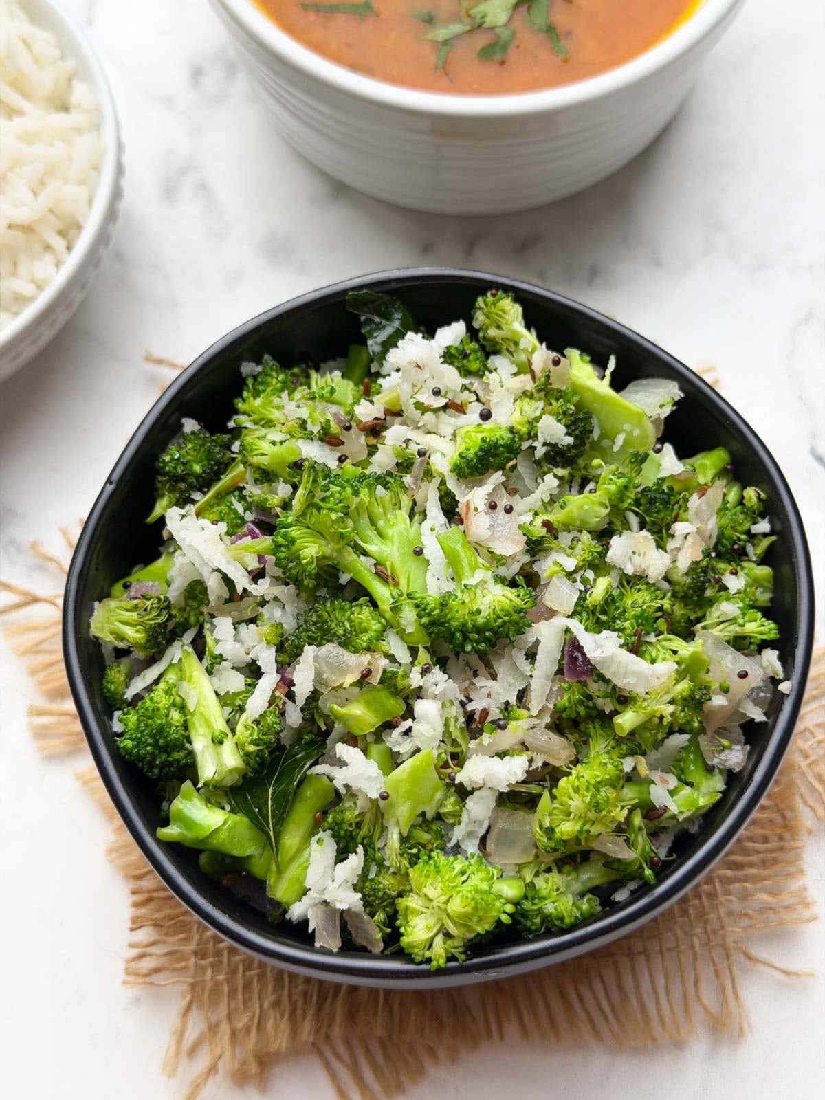 broccoli poriyal served in a black bowl with steamed rice and tomato rasam on the side.
