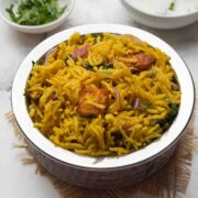 pressure cooker Paneer biryani in a steel serving pot with raita and coriander leaves on the side.