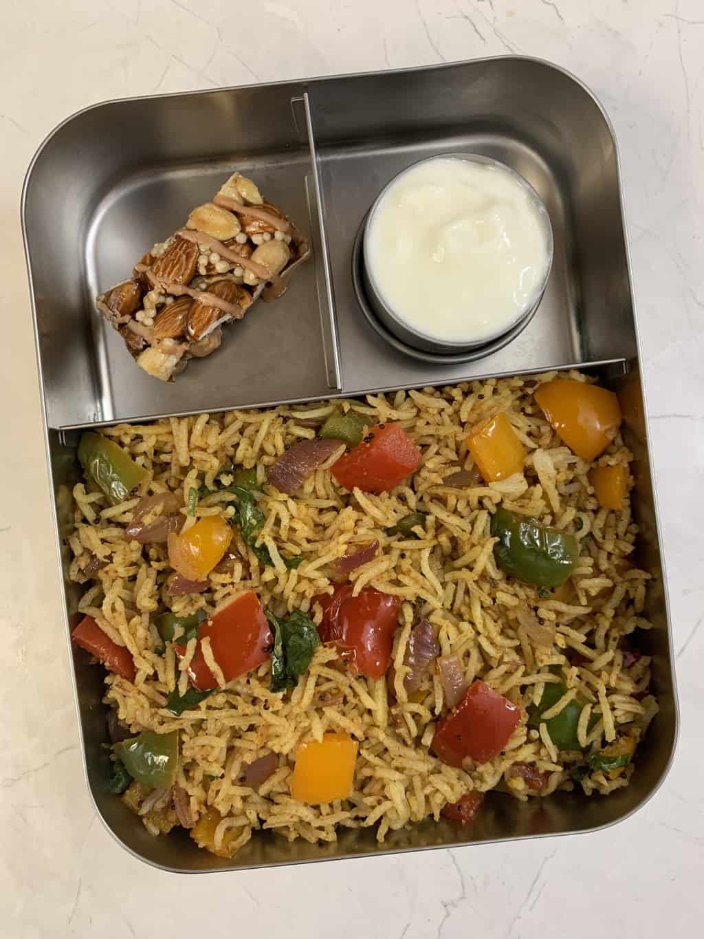 capsicum rice, yogurt and protein bar in bento lunch box.