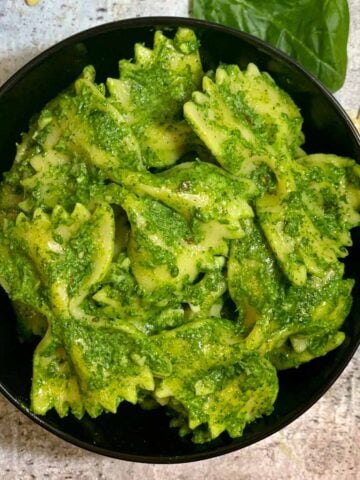 Spinach Pasta served in a black bowl with baby spinach and pasta on side