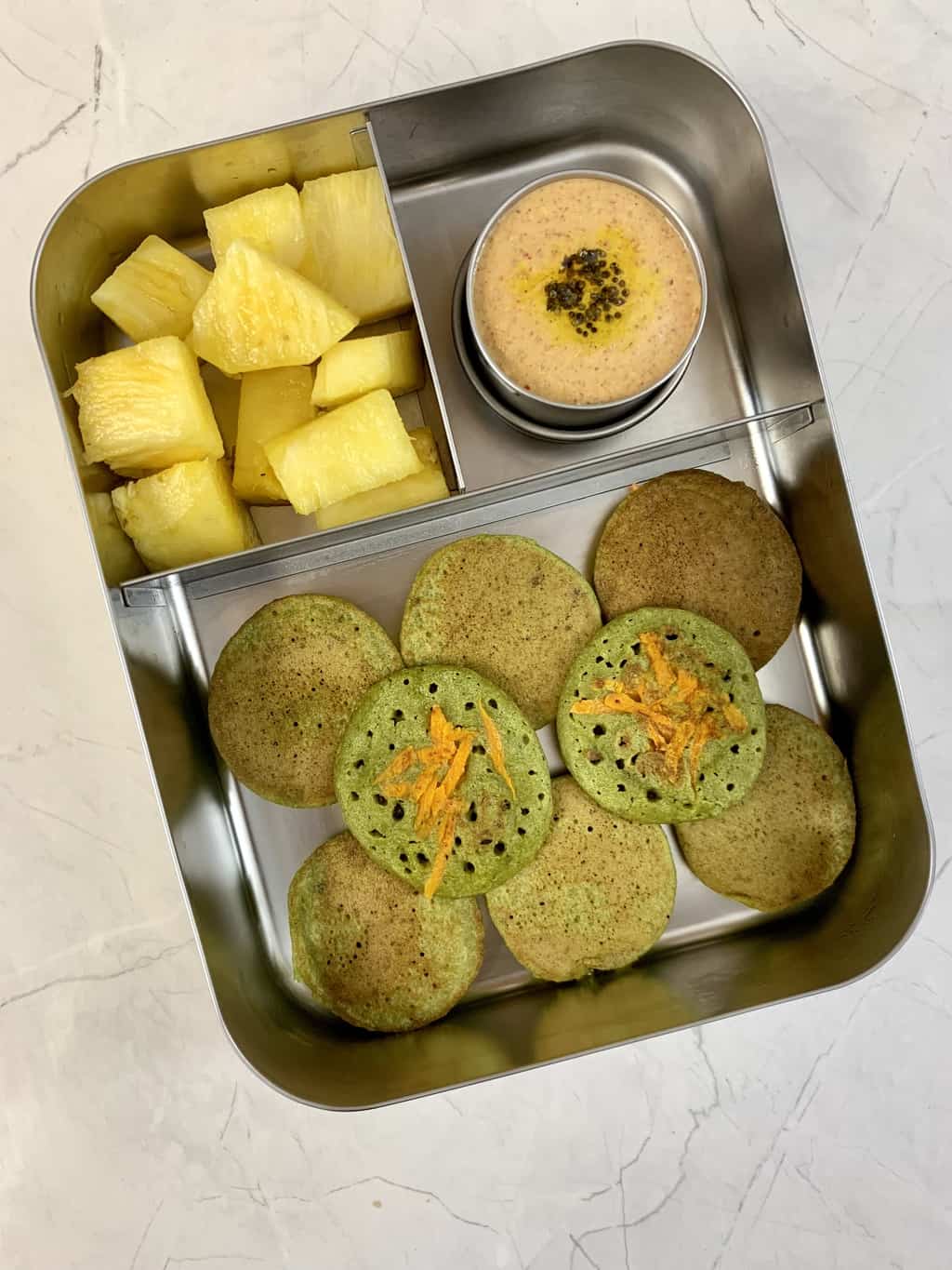 spinach coin dosa, peanut chutney and pineapple in bento steel lunch box.