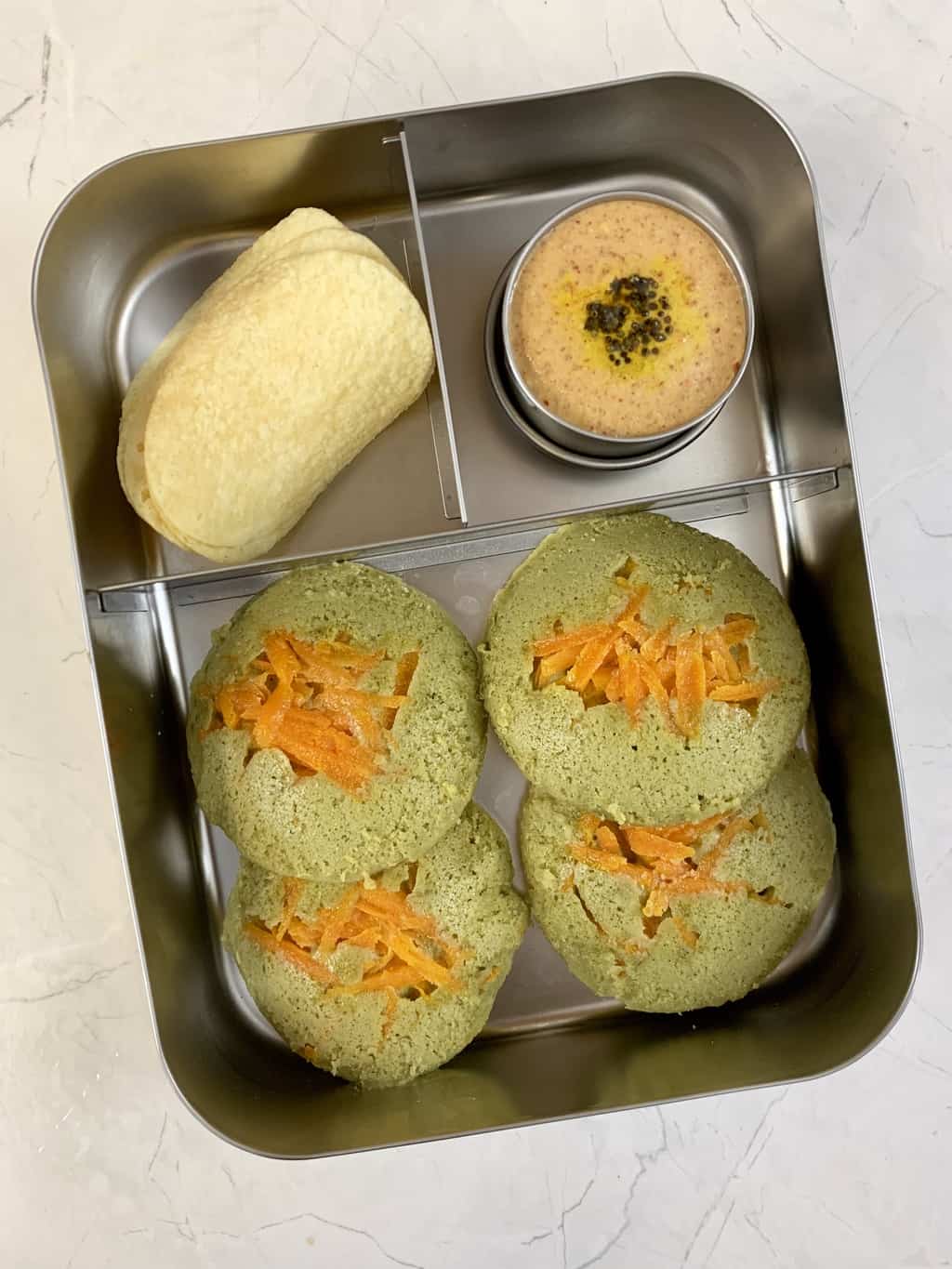 Spinach idli with peanut chutney and chips in bento steel lunch box