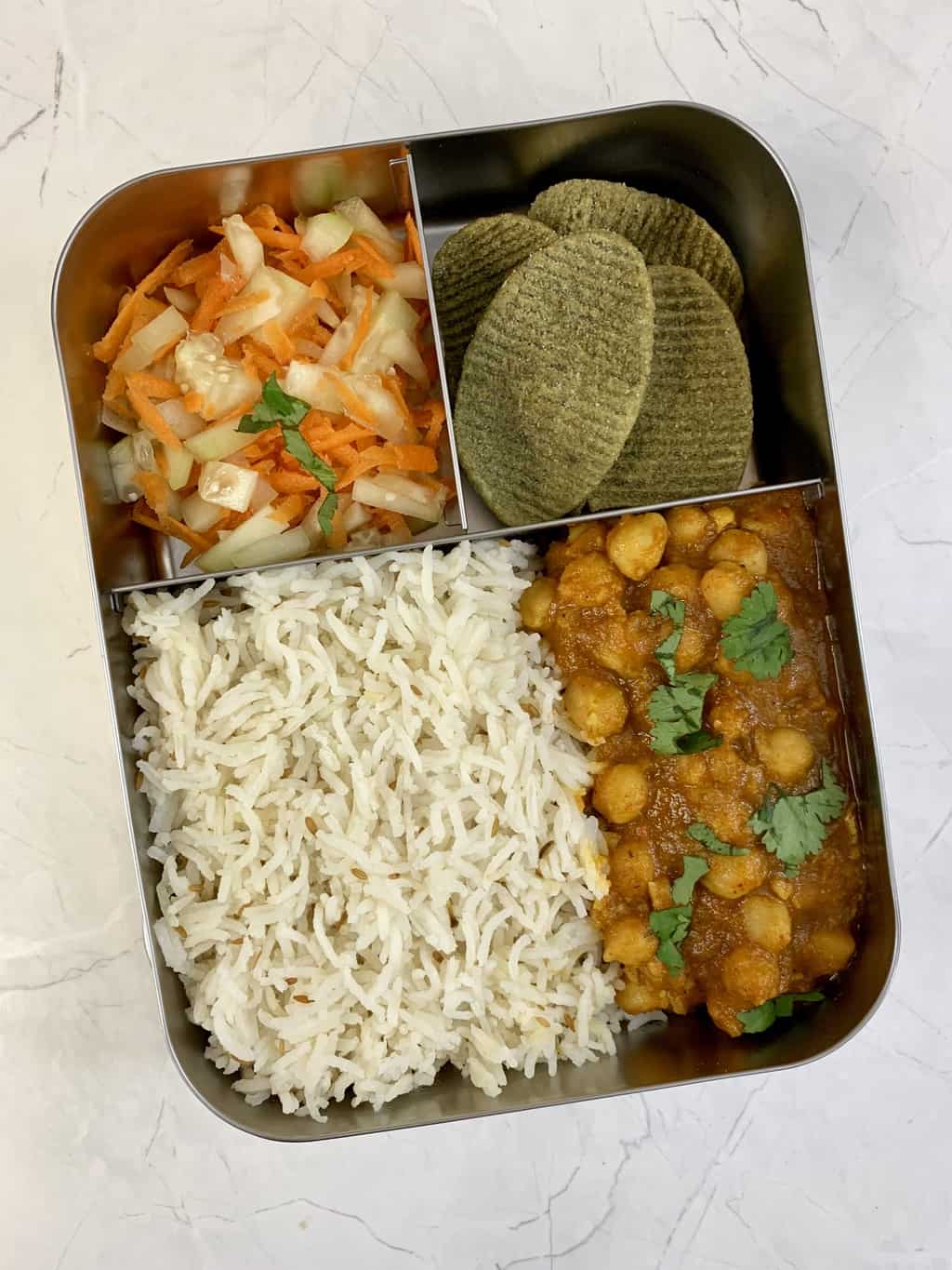 chana masala and jeera rice, salad and kale chips in bento lunch box.