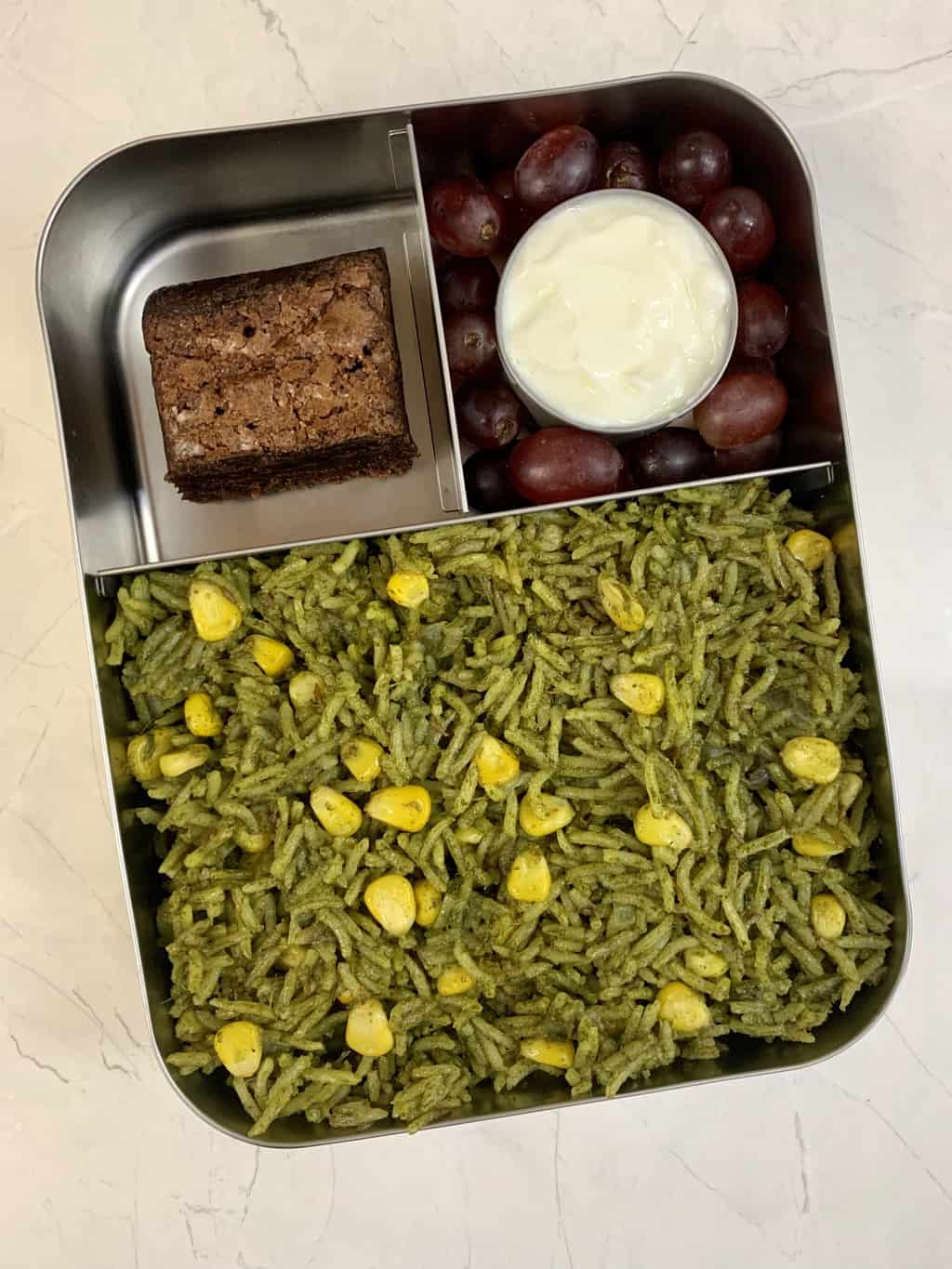 spinach rice, yogurt, grapes and brownie in steel bento lunch box.