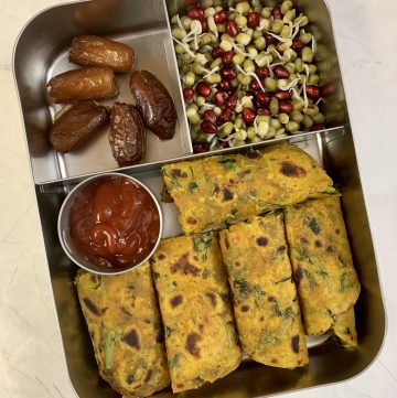 Methi paratha with ketchup, sprouts salad and dates in steel lunch box.