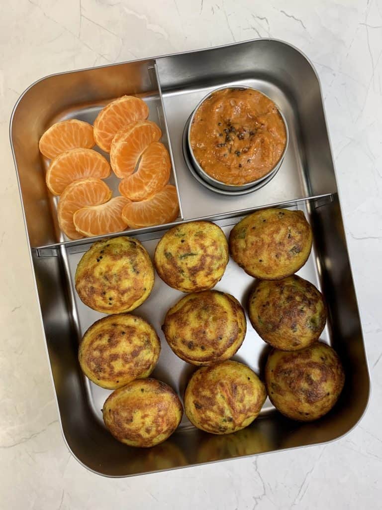 vegetable paniyaram in kids lunch box with onion chutney and orange on the side