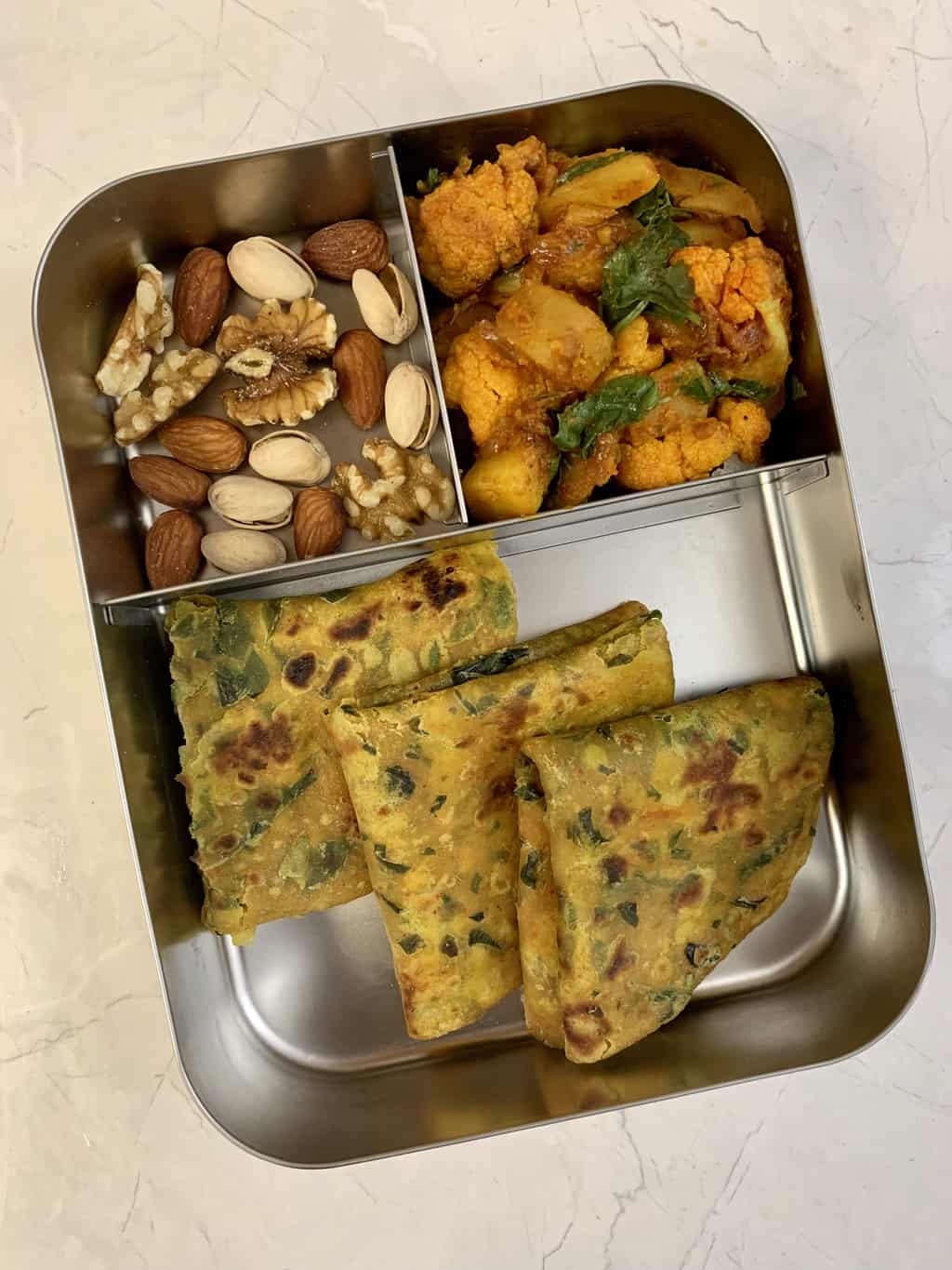 drumstick leaves paratha, aloo gobi and nuts in bento steel lunch box.