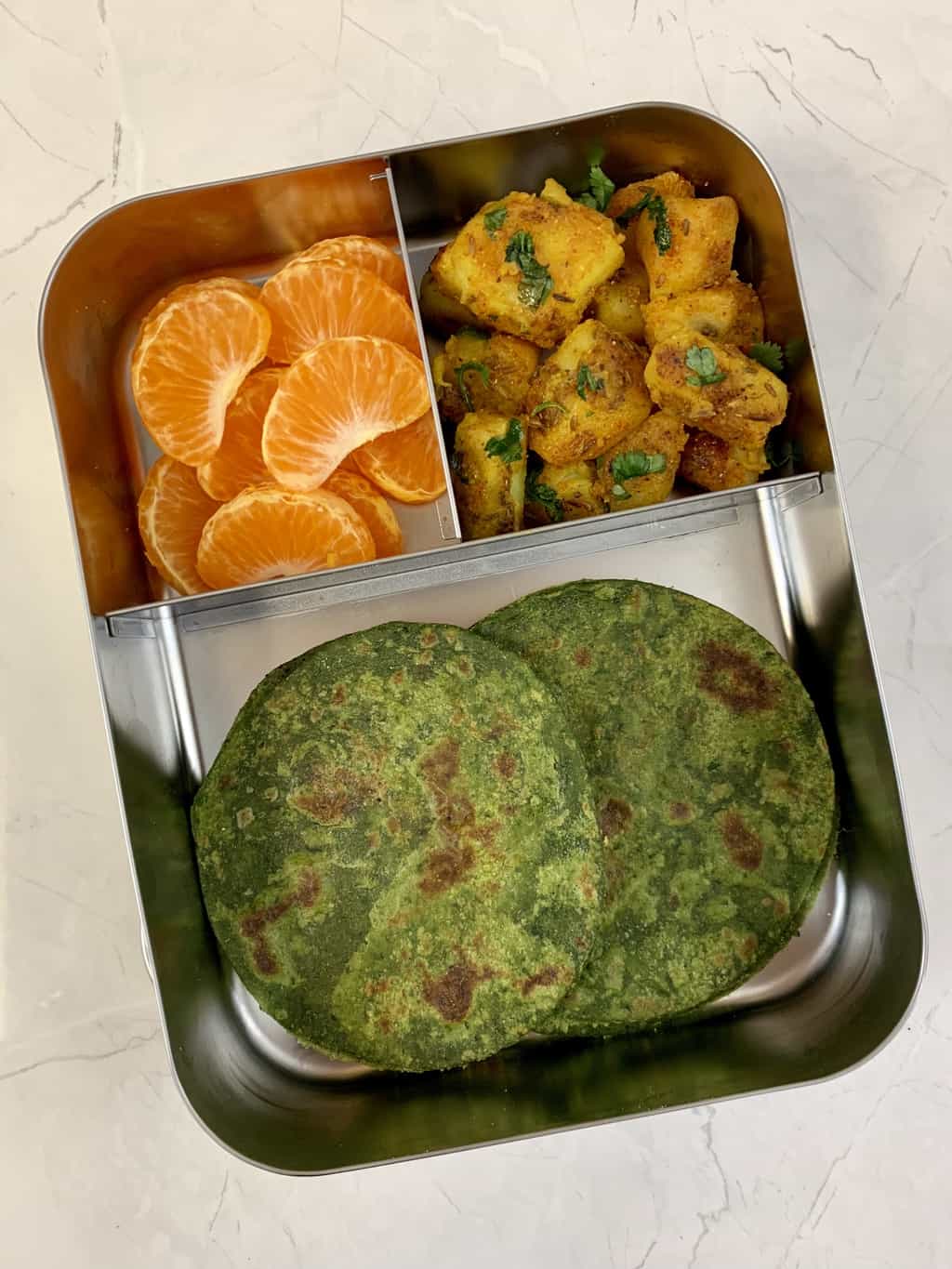 spinach chapati with aloo sabzi and orange in bento steel lunch box