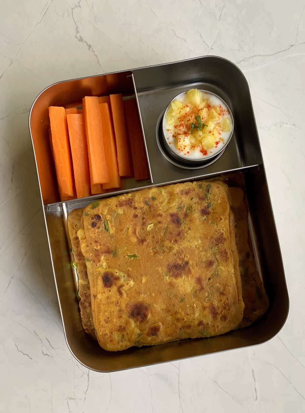 Dal paratha with pineapple raita and carrot sticks in steel bento lunch box