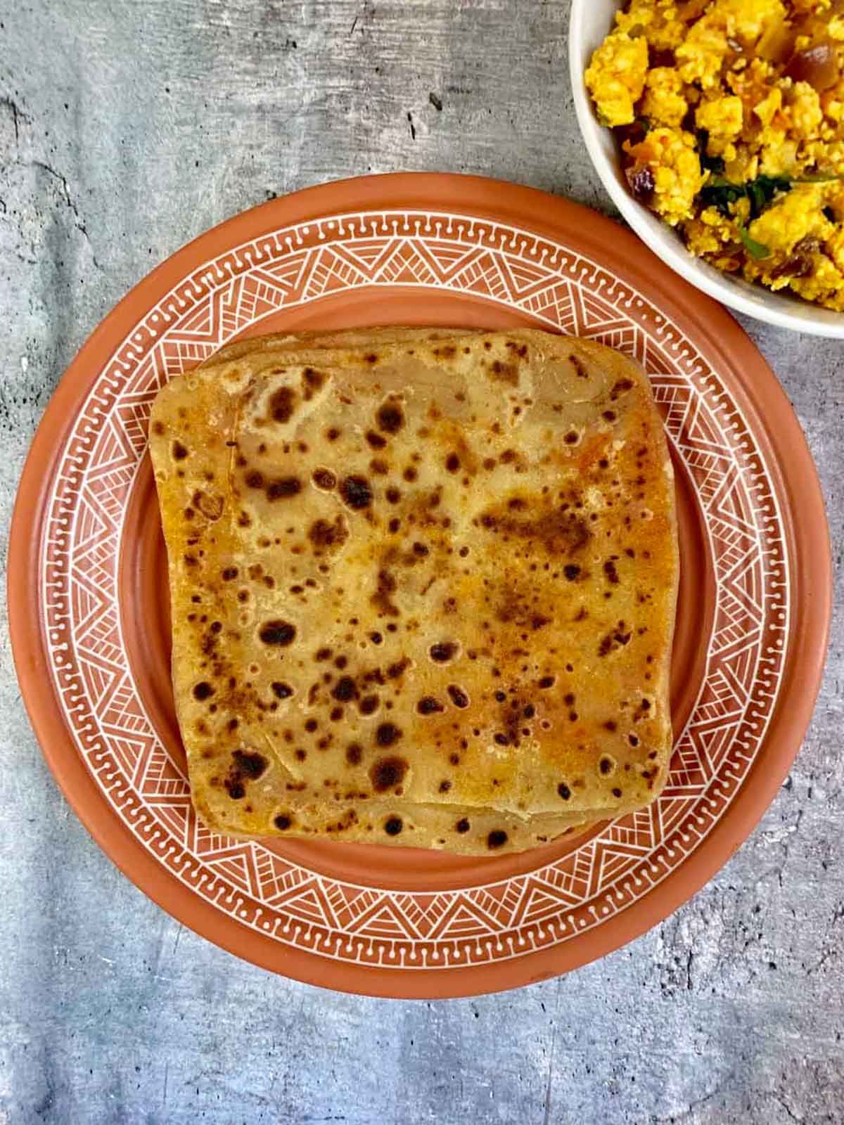 ajwain paratha served on a plate with paneer bhurji on side.