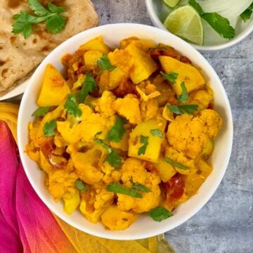 Aloo Gobi recipe served in a bowl with lemon wedges on the side