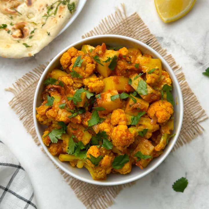 aloo gobi sabzi served in a bowl with garlic naan and lemon wedge on the side