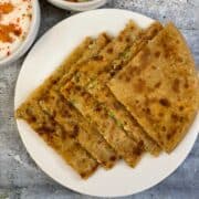 Stuffed Broccoli Paneer Paratha served on a plate with raita and cut cucumber and carrots on the side