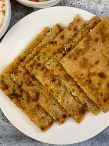 Stuffed Broccoli Paneer Paratha served on a plate with raita and cut cucumber and carrots on the side