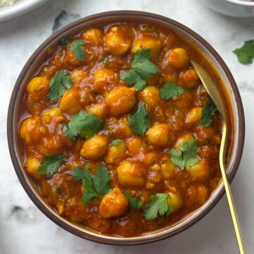 chana masala curry served in a bowl with a spoon and rice, and salad on the side