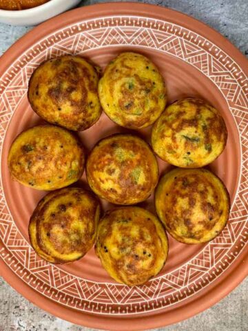 vegetable paniyaram served on a plate with onion chutney on the side