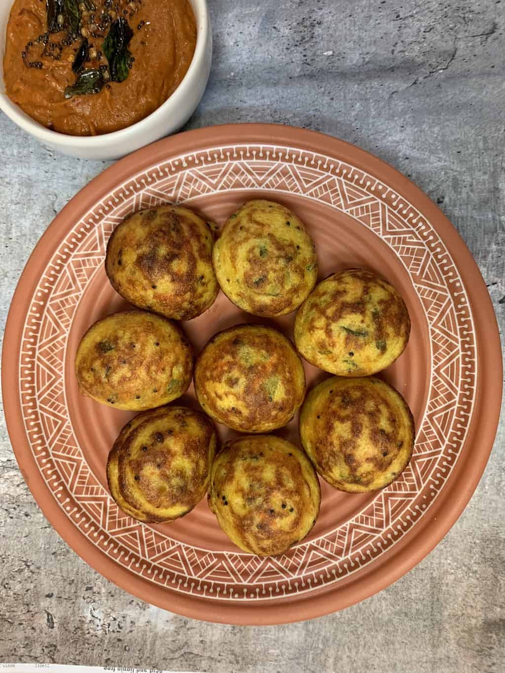 vegetable paniyaram served on a plate with onion chutney on the side