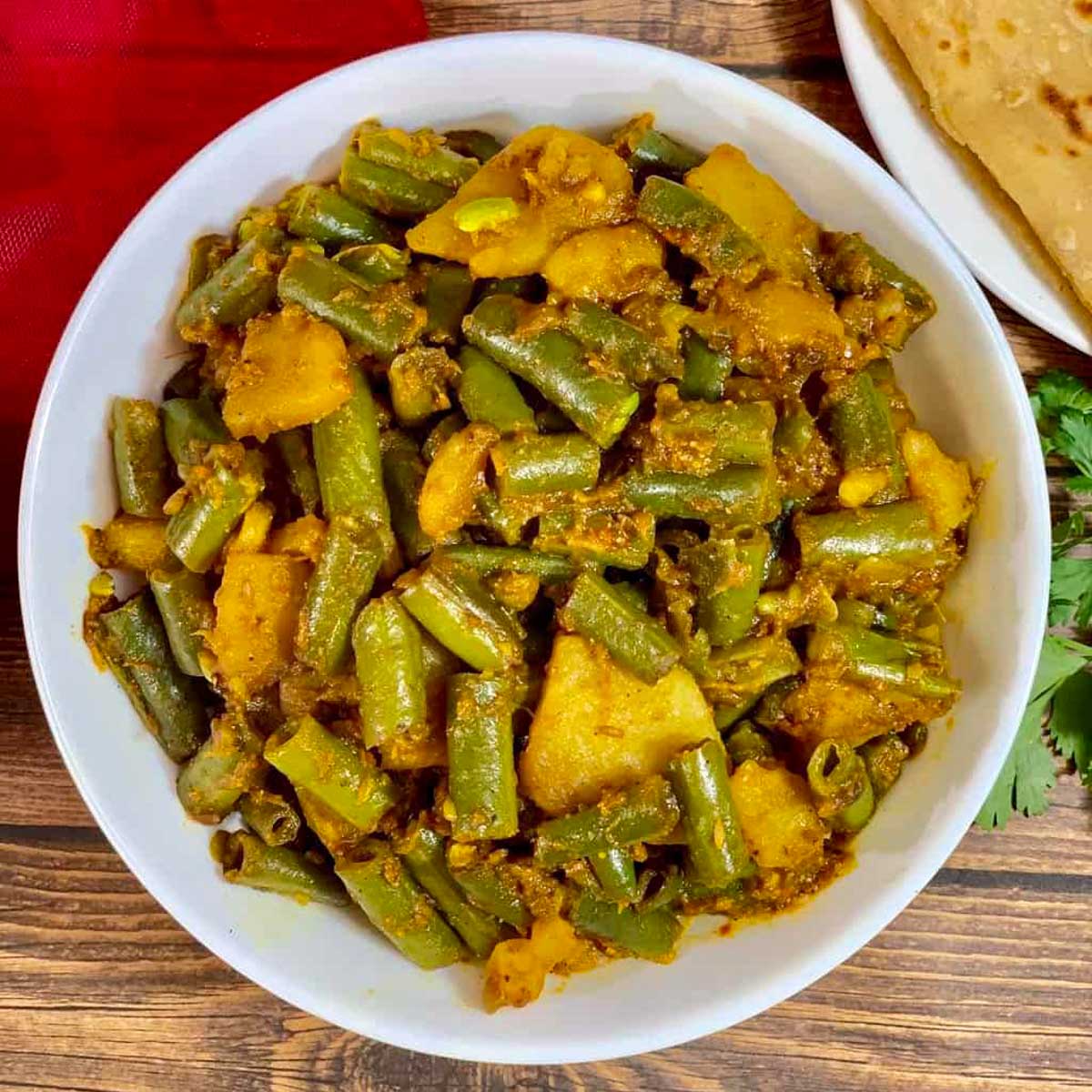 Aloo beans served in a white bowl with chapati on the side