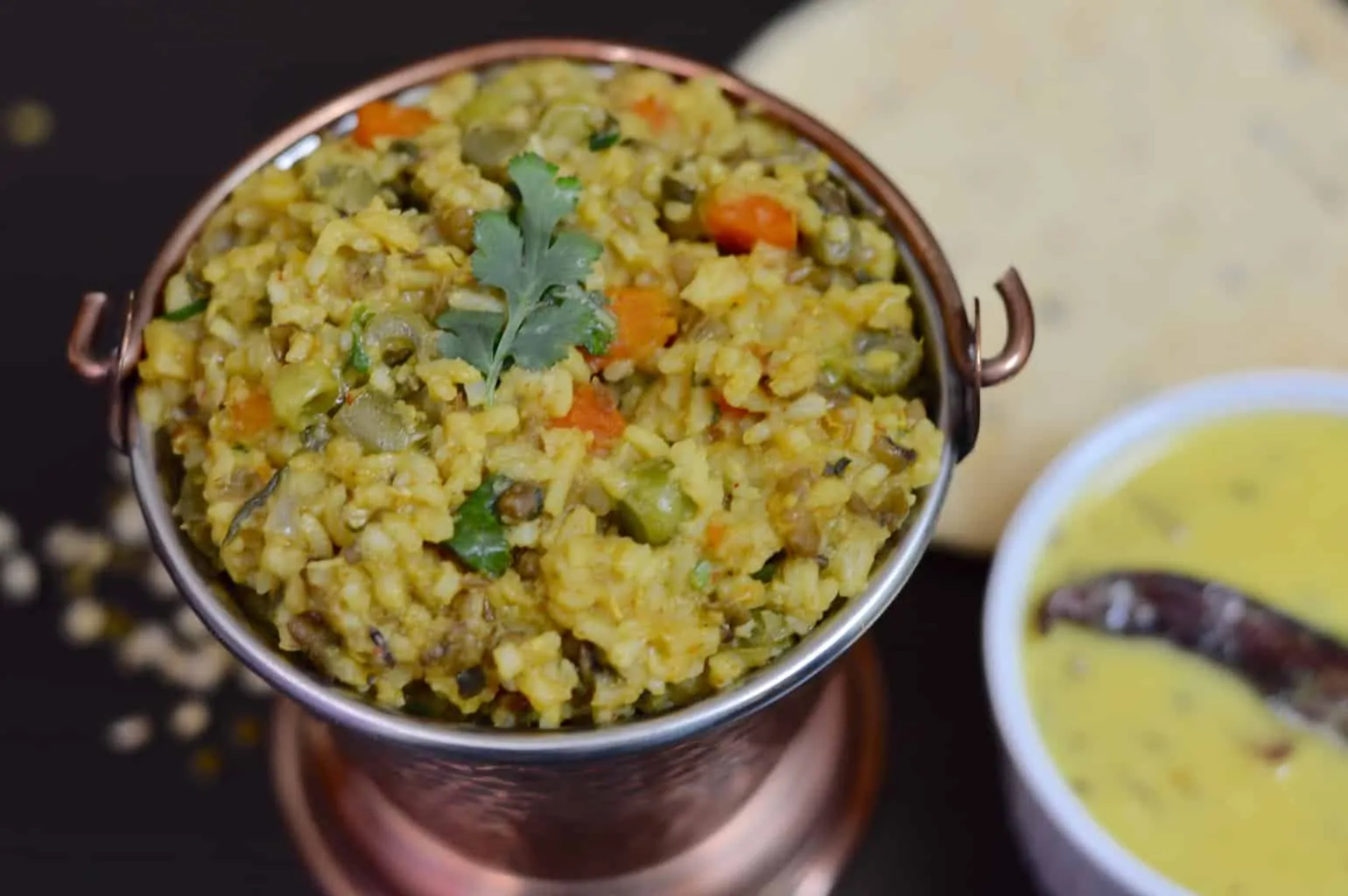 vegetable khichdi served in a container with kadhi on the side