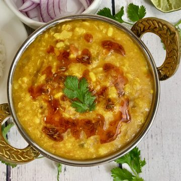Panchmel dal (Panchratna Dal pressure cooker) served in a kadai with tempering on the top and lemon wedge and onions on the side