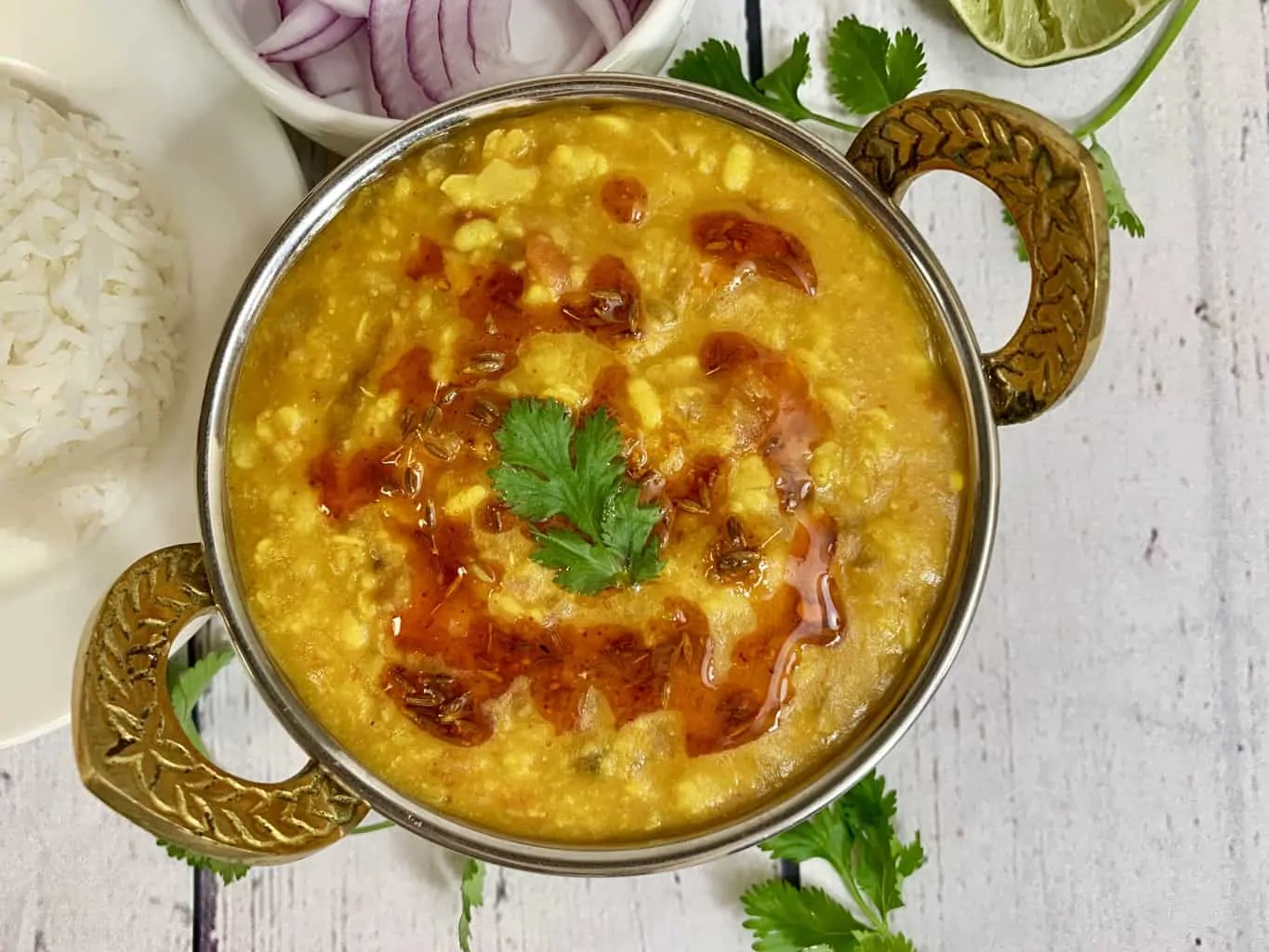 Panchmel dal (Panchratna Dal pressure cooker) served in a kadai with tempering on the top and lemon wedge and onions on the side