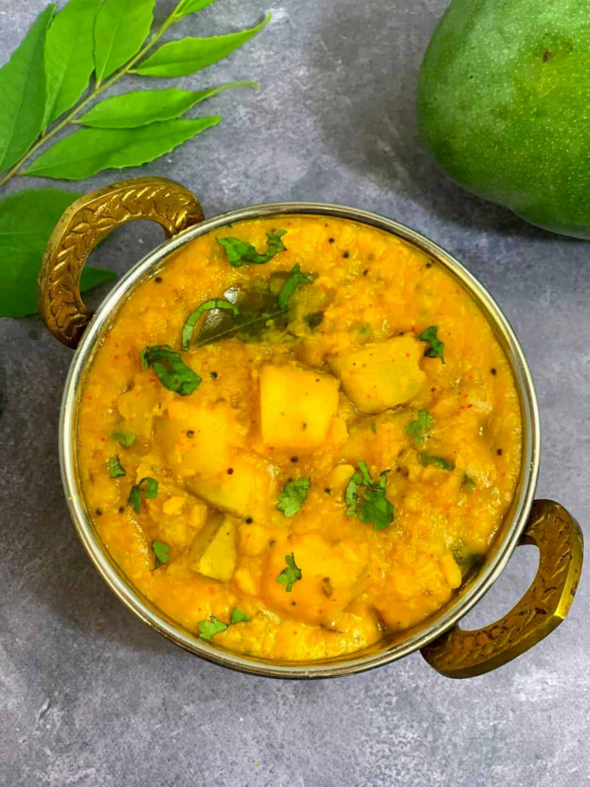 Raw mango dal served in a kadai garnished with cilantro