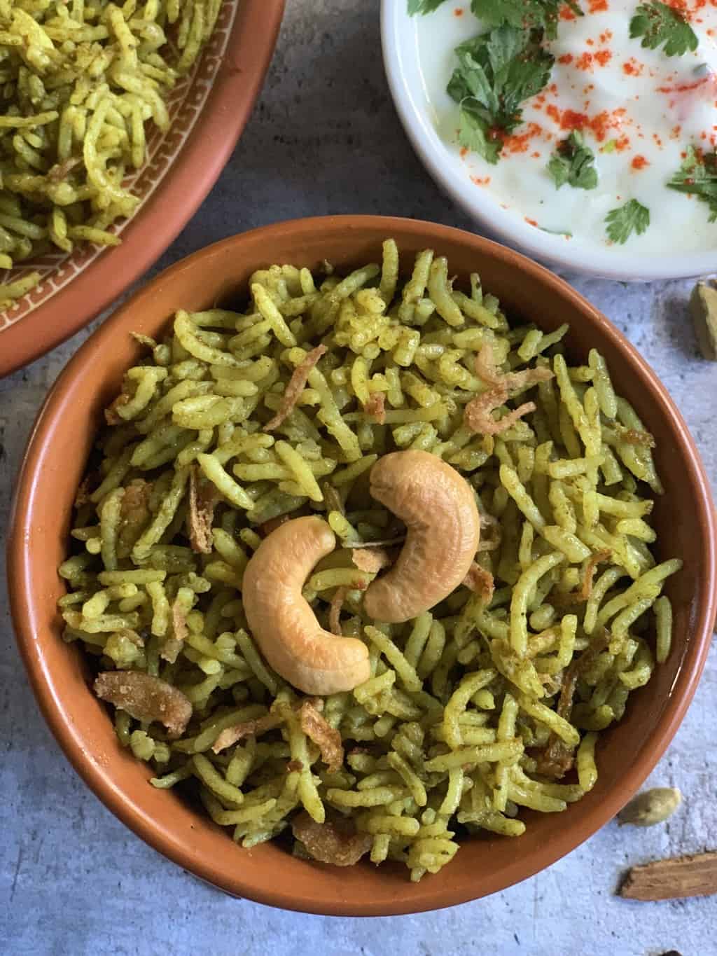 palak biryani served in a bowl garnished with roasted cashews with a side of onion tomato raita