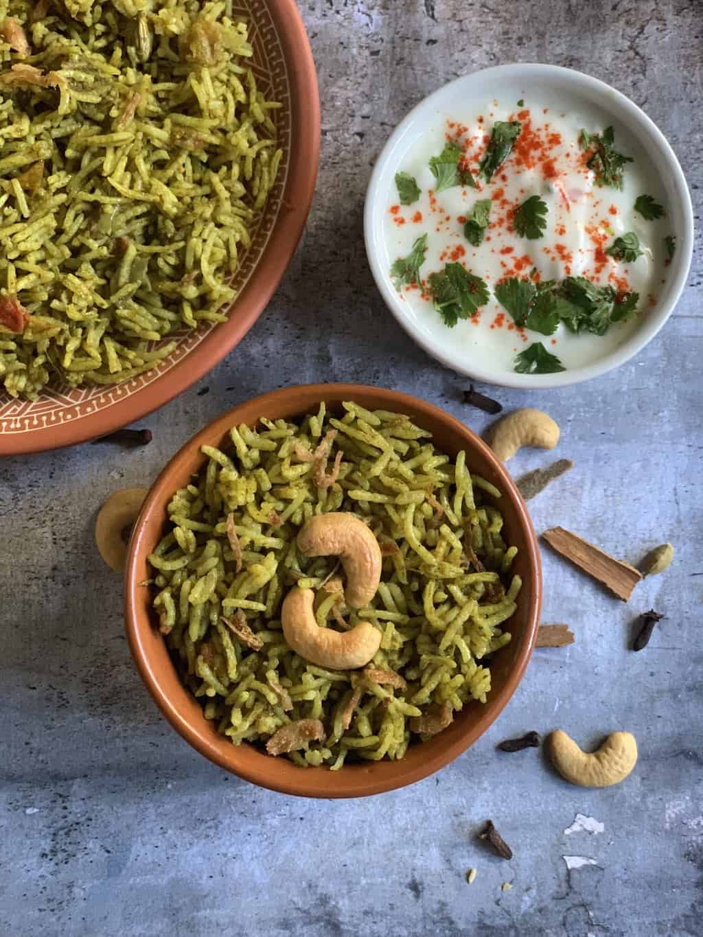 palak biryani served in a bowl garnished with roasted cashews with a side of onion tomato raita