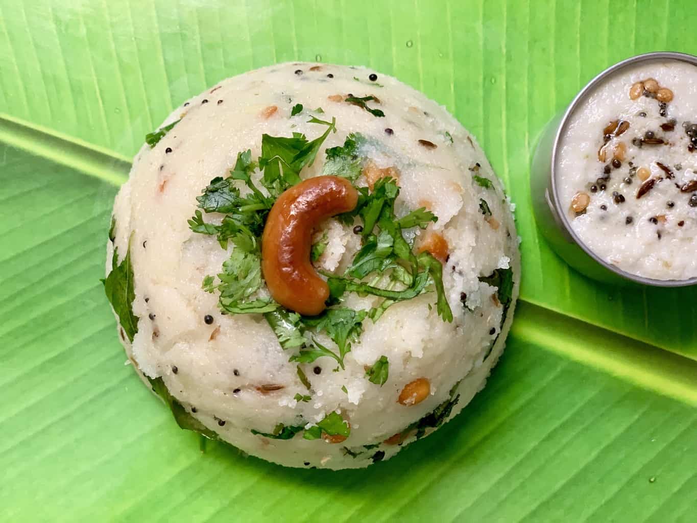 rava upma recipe served on a banana leaf garnished with roasted cashew and coriander leaves with side of coconut chutney