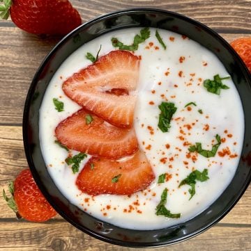 strawberry raita served in a bowl topped with cut strawberries and cilantro