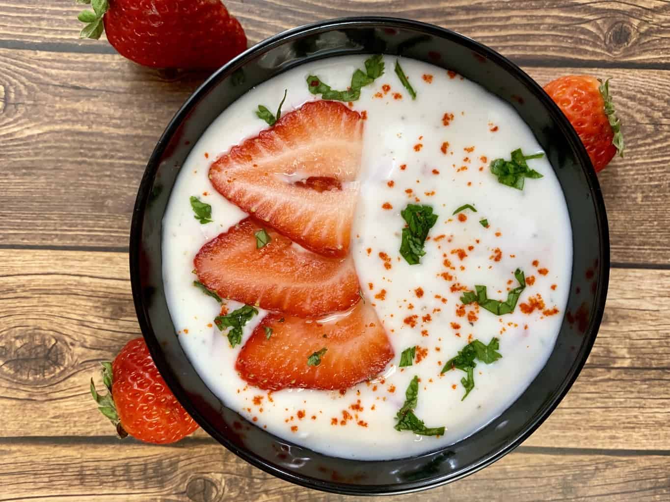 strawberry raita served in a bowl topped with cut strawberries and cilantro