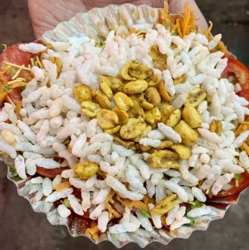 tomato slice chaat on a paper plate topped with puffed rice and congress kadlekai