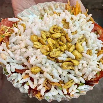 tomato slice chaat on a paper plate topped with puffed rice and congress kadlekai
