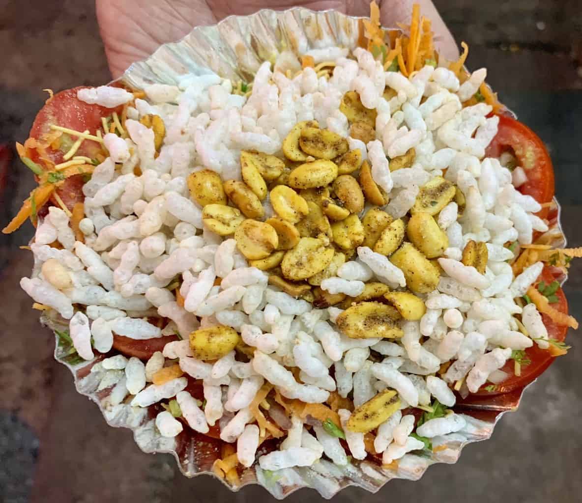 tomato slice chaat on a paper plate topped with puffed rice and congress kadlekai