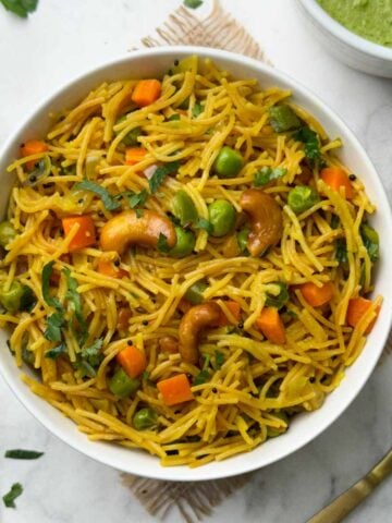 vermicelli upma served in a white bowl with a spoon and green coconut chutney on the side