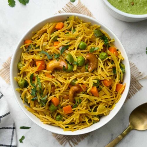 vermicelli upma served in a white bowl with a spoon and green coconut chutney on the side