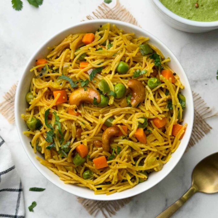 vermicelli upma served in a white bowl with a spoon and green coconut chutney on the side