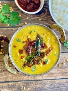 dal tadka served in a kadai with tempering on top and side of rice and pickle