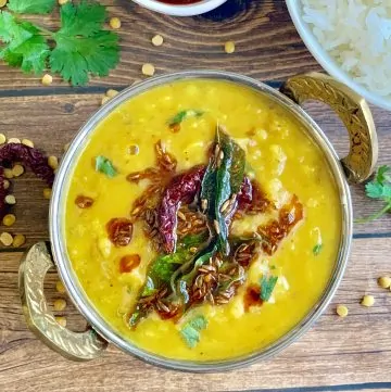 dal tadka served in a kadai with tempering on top and side of rice and pickle