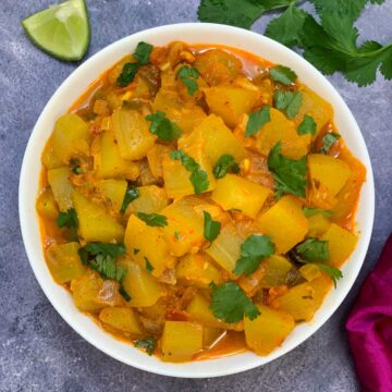 lauki ki sabji served in a wite bowl garnished with coriander leaves and lemon wedge on side