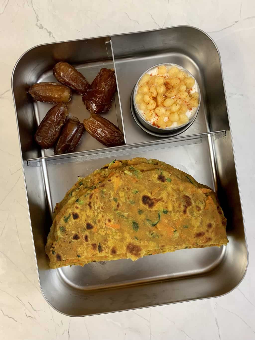 zucchini carrot paratha, boondi raita and dates in bento steel lunch box.