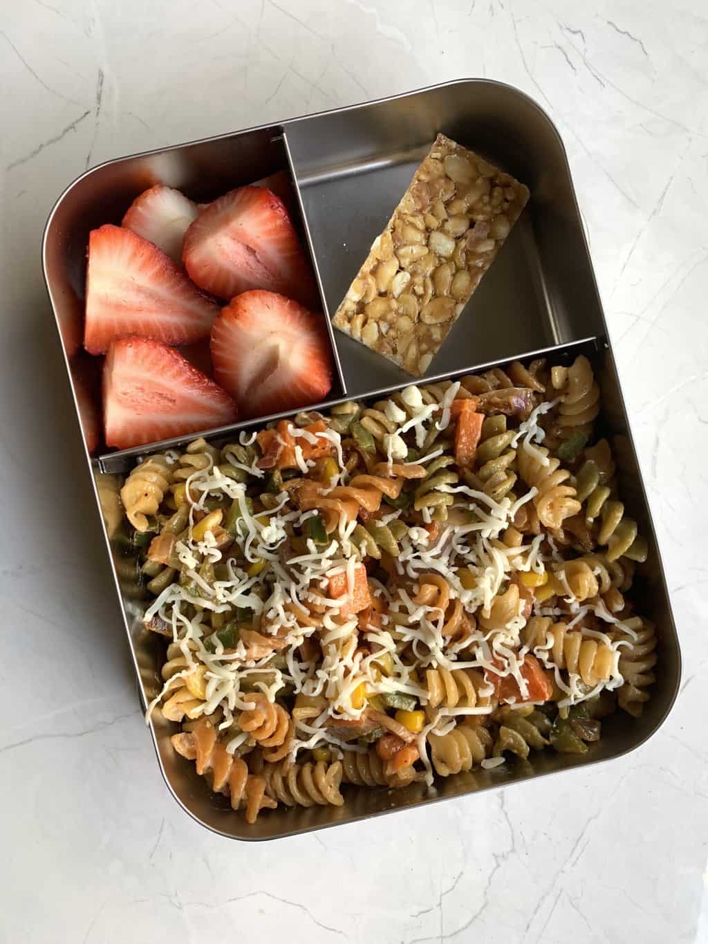 cheesy mayonnaise pasta, peanut chikki and strawberries in bento steel lunch box.