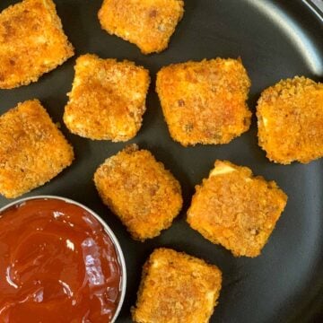 paneer popcorn served in a black plate with tomato ketchup on side