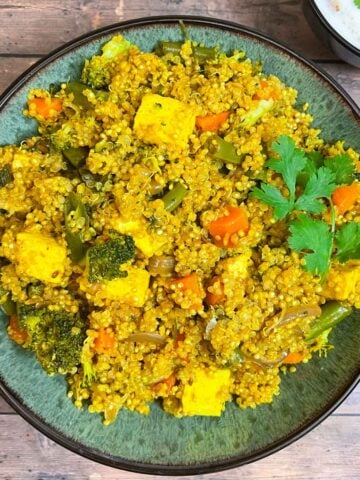 vegetable quinoa biryani served in a bowl garnished with cilantro and served with side of raita